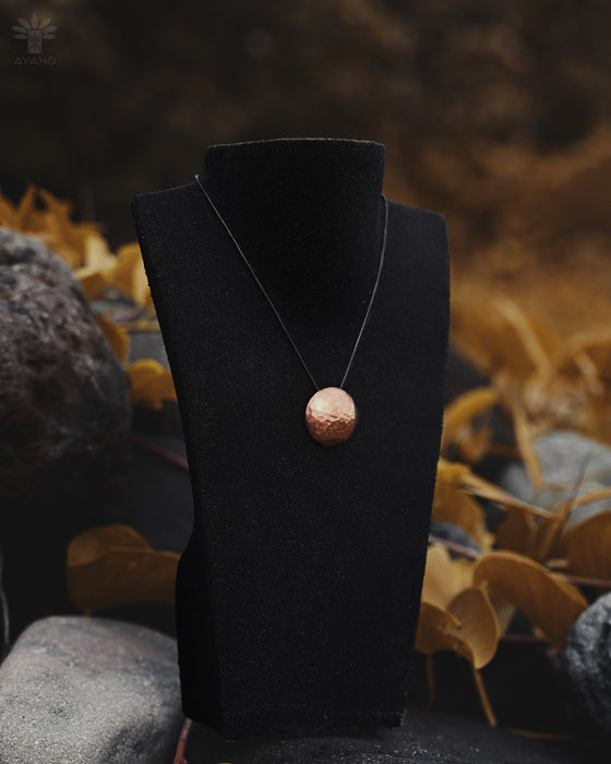 Necklace with a round pendant on a black stand against a natural background with rocks and leaves.