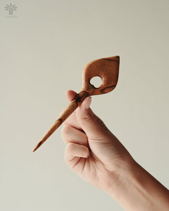 Sleek wooden hair clip shaped like a delicate leaf, carved from sustainable acacia wood with visible natural grain, holding a twist of blonde hair