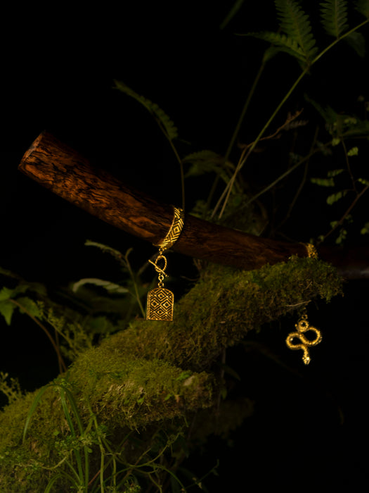 Gold earrings with intricate designs hanging from a branch with green foliage.