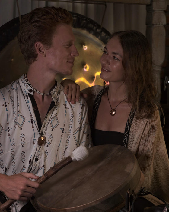 Two people sitting together with a wooden drum in a warm, indoor setting.