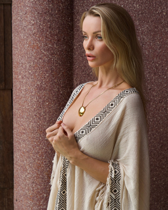 Woman wearing a beige and black patterned garment against a textured wall.