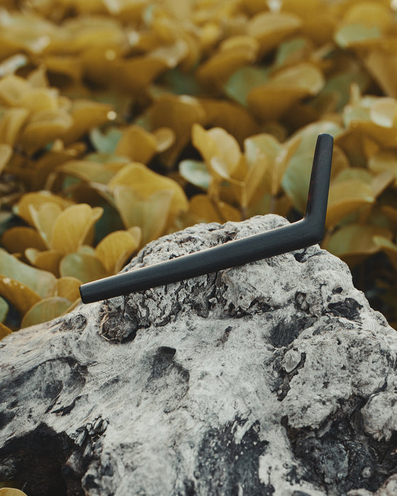 Handcrafted ceremonial pipe carved from solid rosewood with natural wood patterns, displayed against tropical leaves background