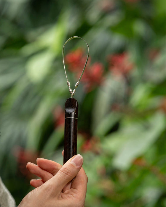 Sustainable bamboo tongue scraper with smooth rounded edge, placed beside a toothbrush and natural toothpaste."