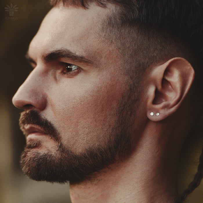 Pair of sleek flat-head stud earrings in gold and silver tones arranged on marble surface, showcasing their smooth circular design and versatile neutral colors.