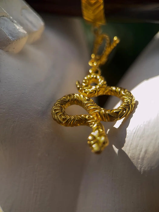Gold snake-shaped pendant on a white surface