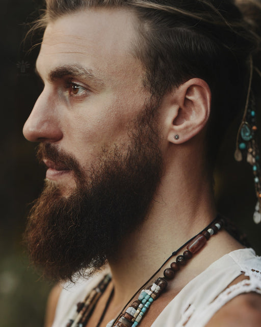 Macro shot of intricate patterned stud earrings catching light, showcasing their textured metalwork and sparkling center stones against a velvet backdrop