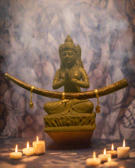 Statue of a seated figure with a large curved object in a tropical setting