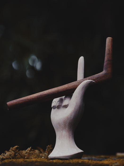 Wooden sculpture of a hand holding a stick against a dark background