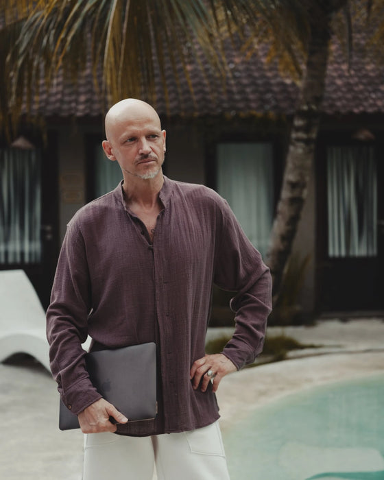 Man holding a laptop by a pool with palm trees and a building in the background
