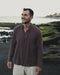 Man in a brown boho shaman cotton shirt standing by a tropical pool holding a laptop, calm retreat setting