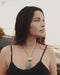 Woman wearing a black tank top with a necklace, standing outdoors.
