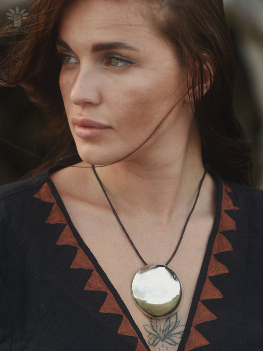 Woman wearing a necklace with a large pendant, looking off to the side.