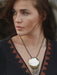 Woman wearing a necklace with a large pendant, looking off to the side.