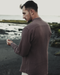 Man standing on a beach wearing a brown shirt with 'AYANO' logo.