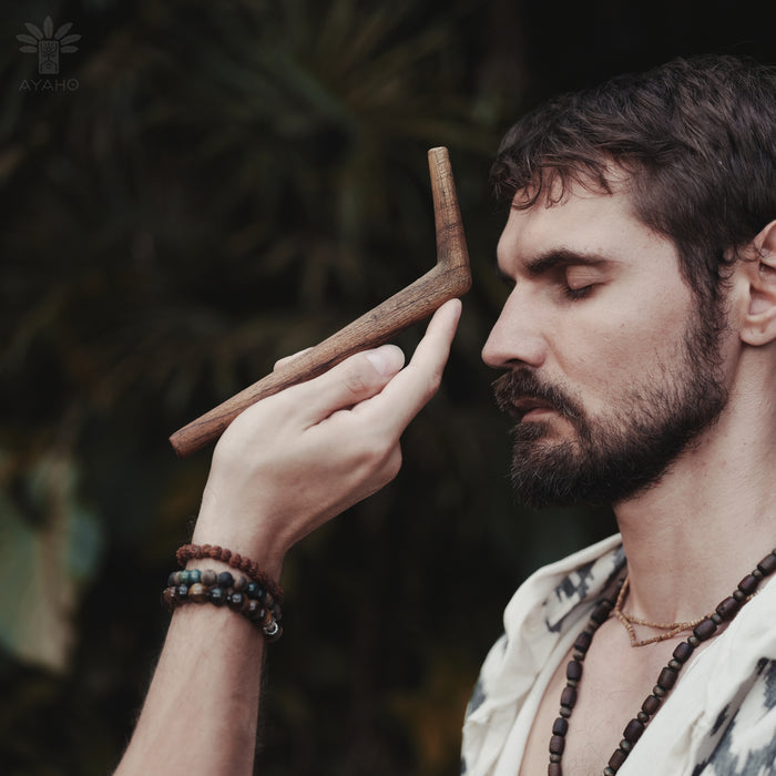 Man holding a wooden tool near his face with a blurred natural background
