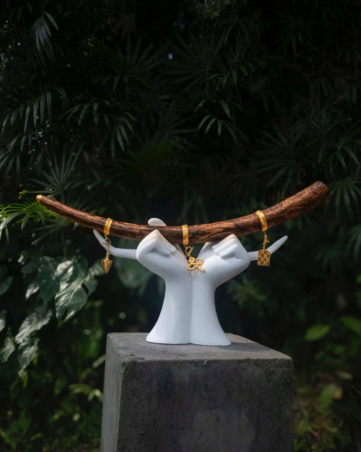 White ceramic hands holding a branch with gold jewelry against a dark green leafy background