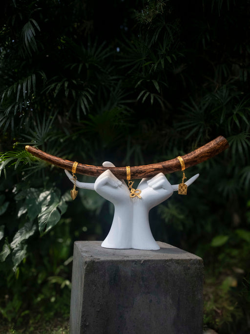 White ceramic hands holding a branch with gold jewelry against a dark green leafy background