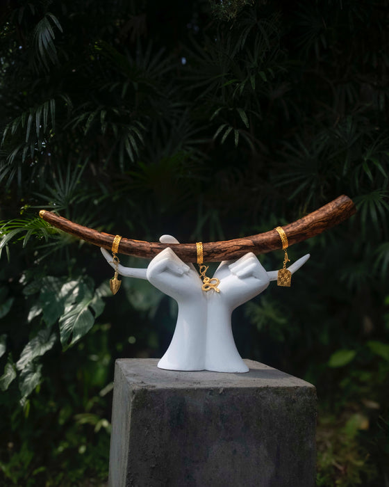 White ceramic hands holding a branch with gold jewelry against a dark green leafy background