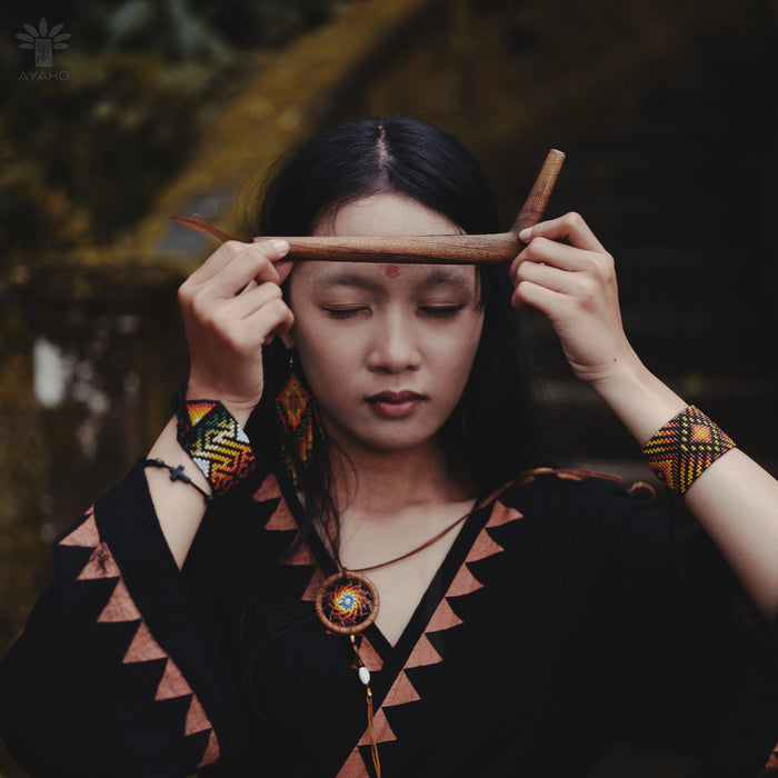 Woman holding two sticks over her eyes with a dark, natural background