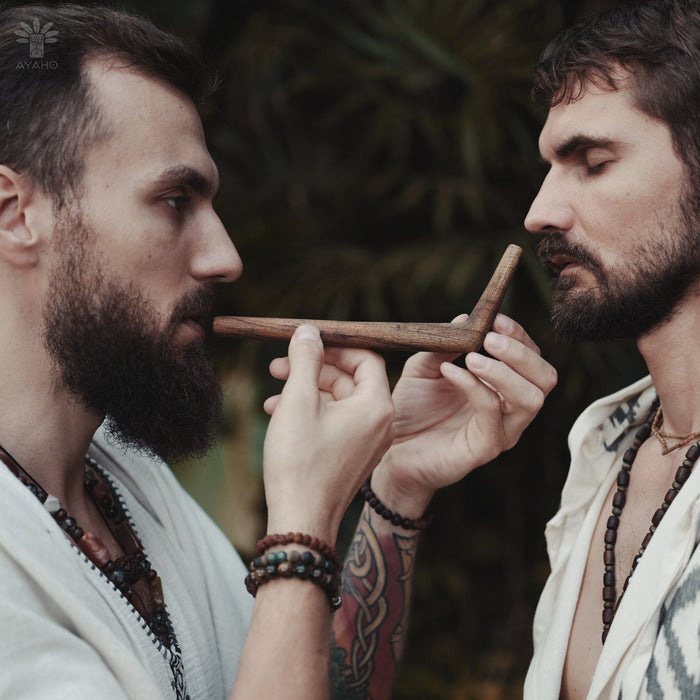 Two men playing a wooden flute against a natural background