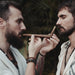 Two men playing a wooden flute against a natural background