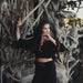 Woman in black outfit posing against a textured wall with natural elements