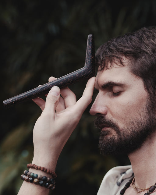 Man holding a wooden tool to his temple against a dark background