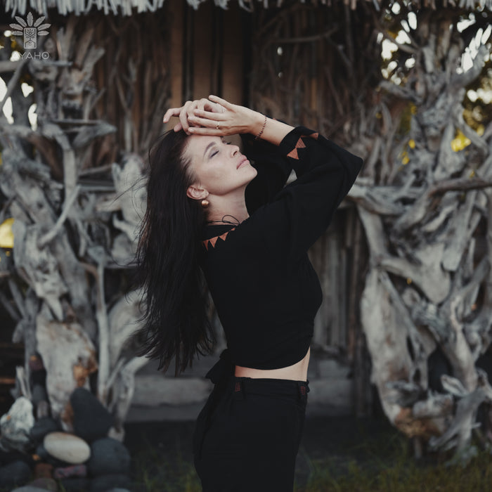 Woman in a black outfit posing with hands on head against a natural background