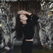 Woman in a black outfit posing with hands on head against a natural background