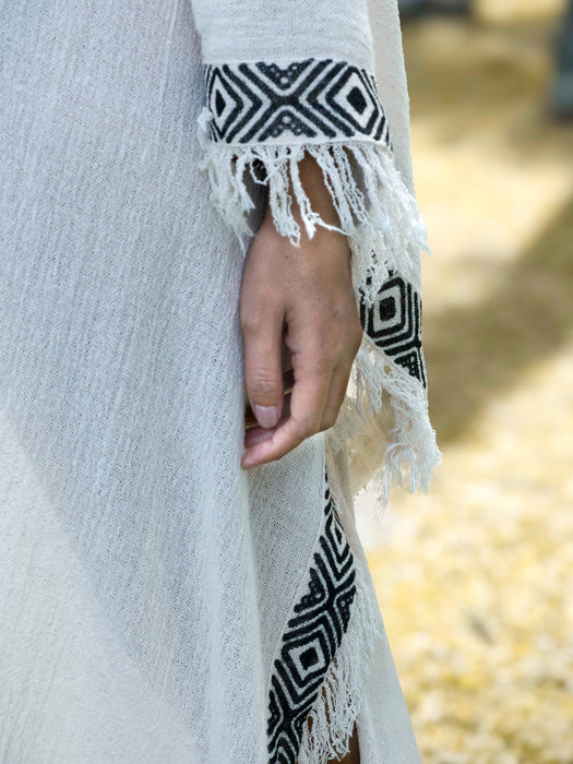 Close-up of a white garment with black geometric patterns and fringes.
