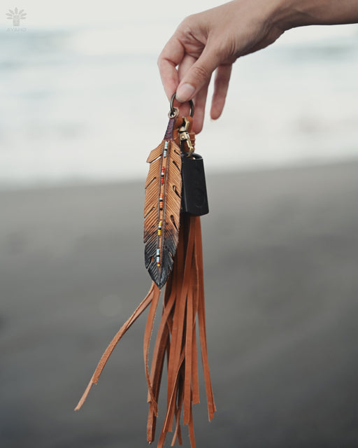 Delicate pheasant feather amulet with copper wire wrapping, suspended from a suede cord over a smudging bowl.