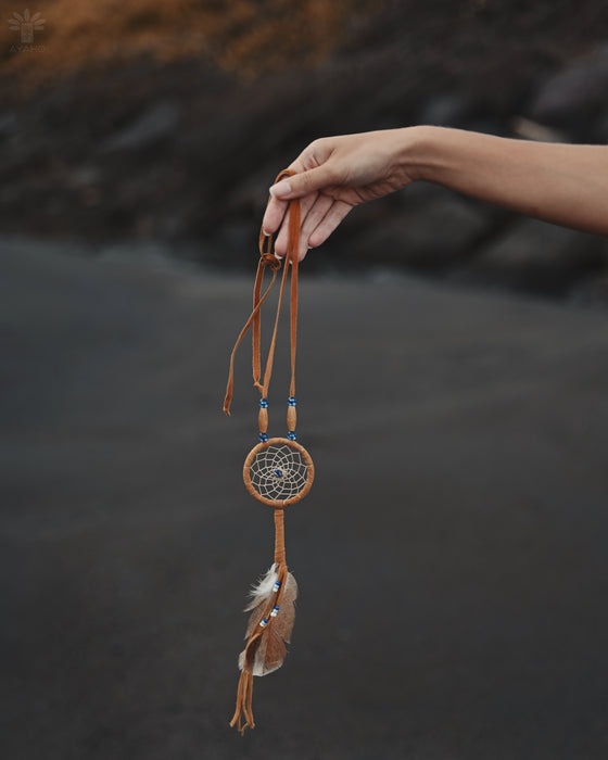 Close-up of a traditional-style dream catcher amulet with amethyst and howlite beadsx, hanging from a car mirror.