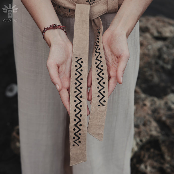 Person holding a belt with decorative patterns against a blurred natural background