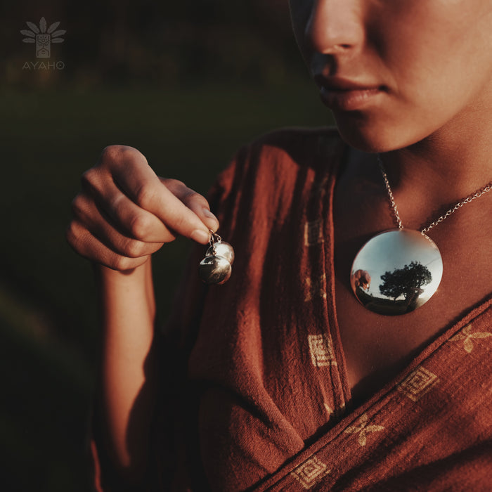 Person wearing a necklace with a reflective pendant, holding another similar pendant.