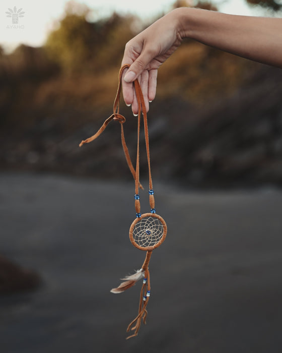 Close-up of a traditional-style dream catcher amulet with amethyst and howlite beadsx, hanging from a car mirror.