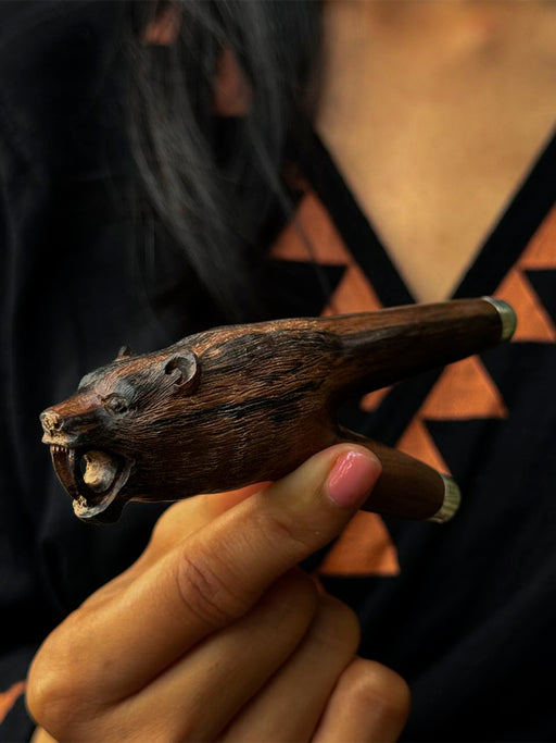 Hand holding a wooden animal-shaped pipe with a blurred background