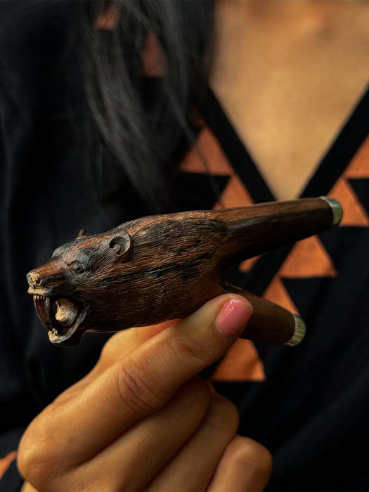 Hand holding a wooden animal-shaped pipe with a blurred background