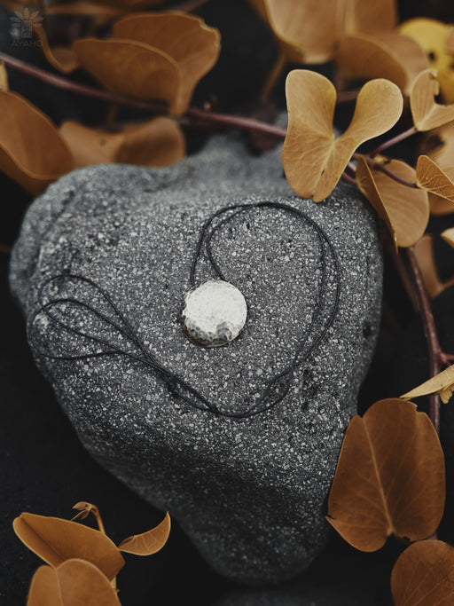 Heart-shaped stone with a necklace on a dark background with brown leaves