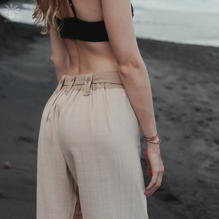 Person wearing a black bikini top and beige pants on a beach.