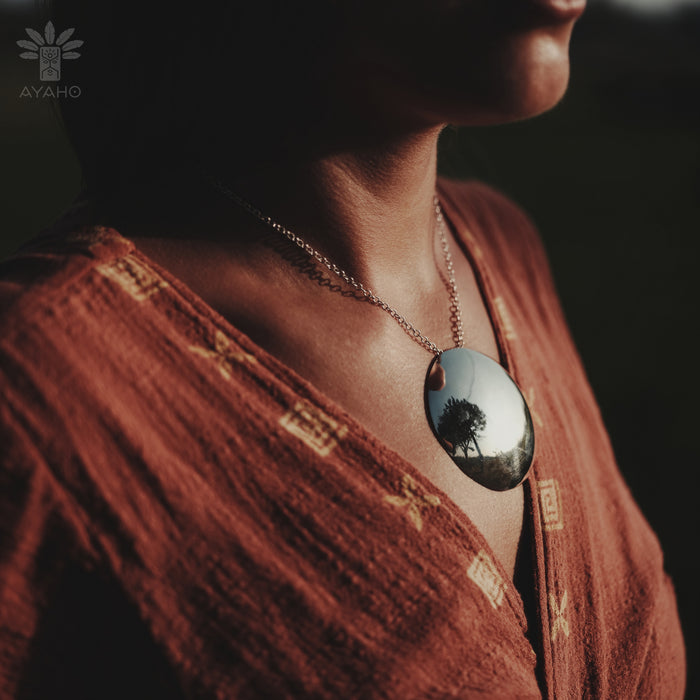 Person wearing a necklace with a reflective pendant, set against a dark background.