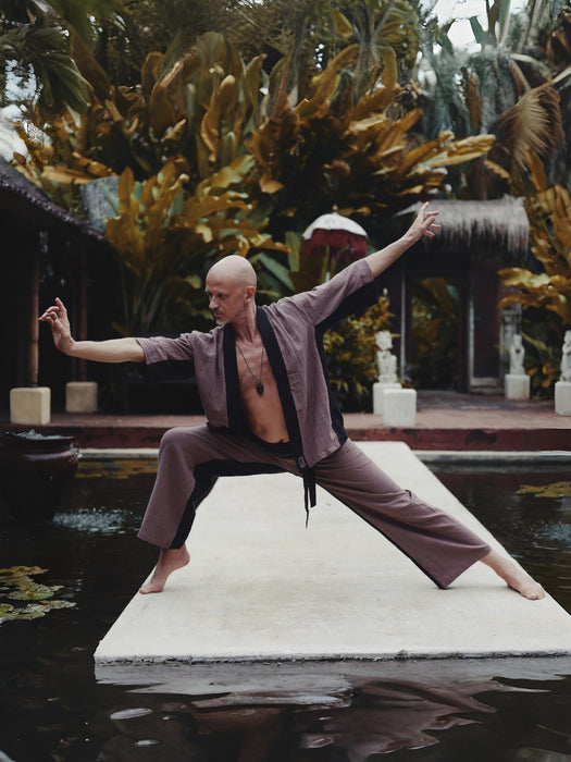 Person in martial arts pose on a platform with lush greenery in the background