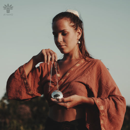Woman in a rust-colored garment holding a small round object against a blurred natural background