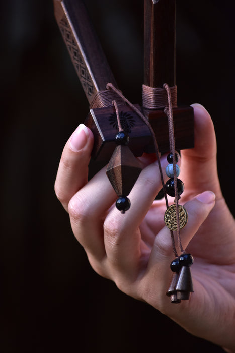 Hand holding a decorative bow with intricate patterns and beads against a dark background
