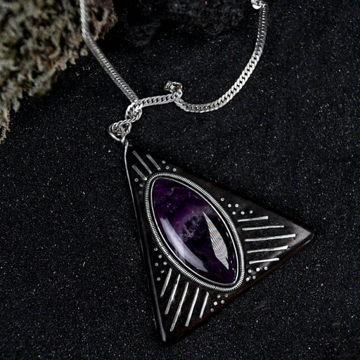 Striking silver triangular amulet with a richly hued amethyst center, designed for harmony, surrounded by symbolic engravings on rosewood for spiritual grounding.