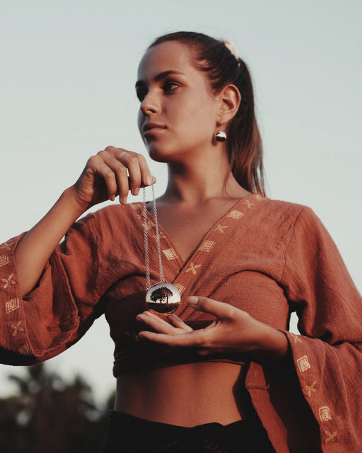 Close-up of the Shaman Mirror Pendant, a symbolic piece of jewelry for spiritual awakening, displayed on a person. The pendant reflects a serene tree landscape, evoking a sense of inner reflection and the journey of self-discovery.