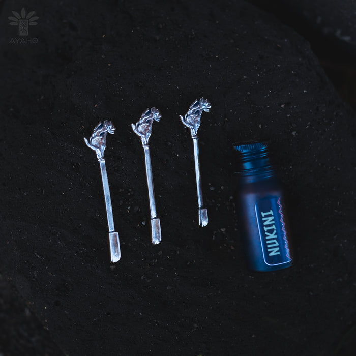 Three silver hair sticks with horse designs and a blue bottle labeled 'Nukini' on a dark background.