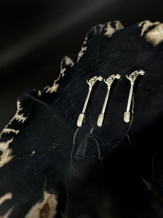 Three silver hairpins on a textured black surface with a patterned fabric background.