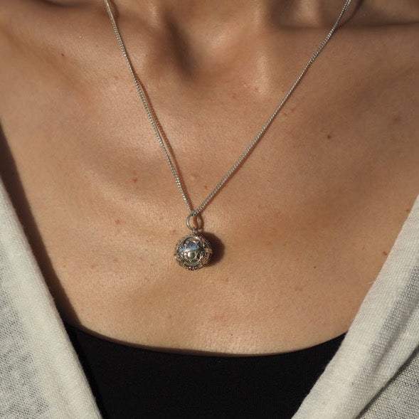 Detailed view of a handcrafted silver harmony bell pendant, serving as a talisman amulet, associated with heart healing and negative energy protection