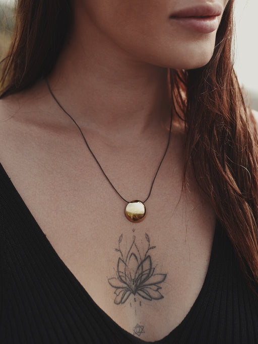 Personalized copper pendant with initials carved near the mirror, laid on handmade paper with ink-dyed fabric.