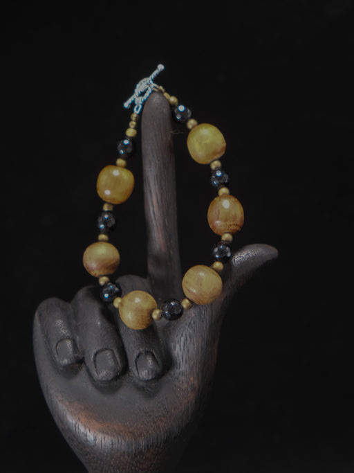 Bracelet with yellow and black beads on a wooden hand sculpture against a dark background
